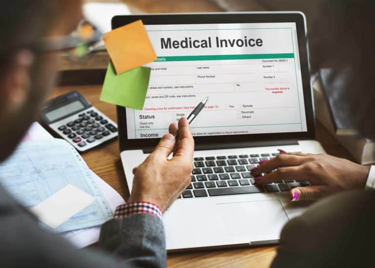 People review managed care reimbursement with a medical invoice pulled up on a laptop