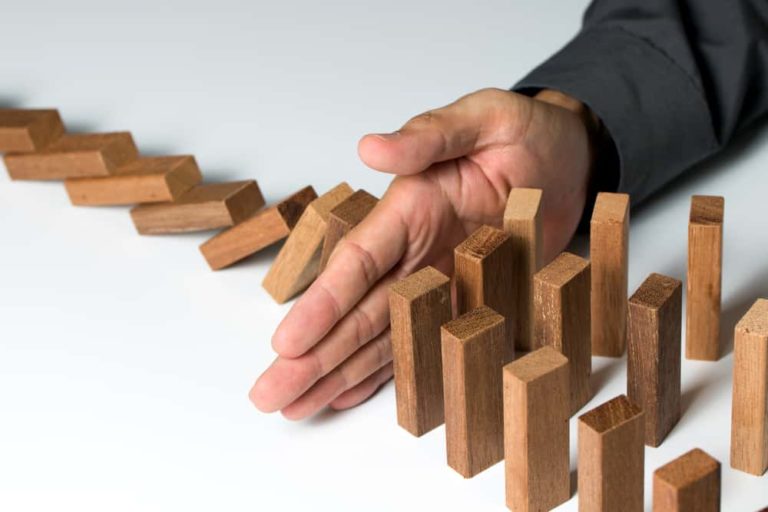 A man stops a line of falling blocks from knocking over more blocks, to illustrate how stop-loss works in health insurance.